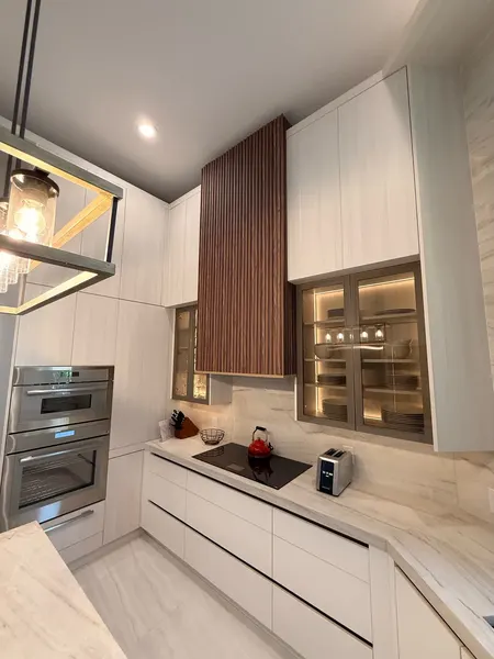 Walnut slat range hood between handleless uppers and lit glass cabinets.