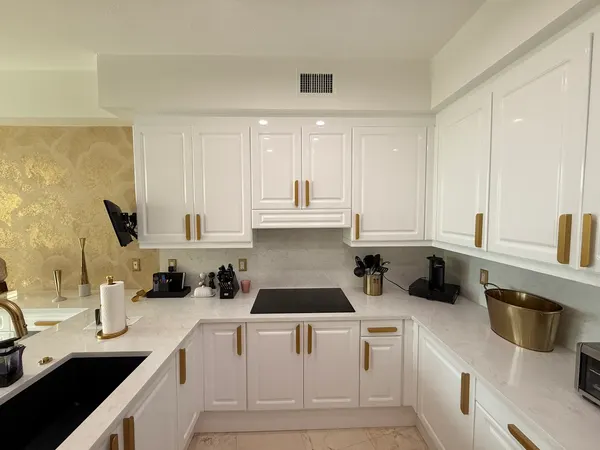 Glossy white raised-panel uppers and lowers with long gold pulls.