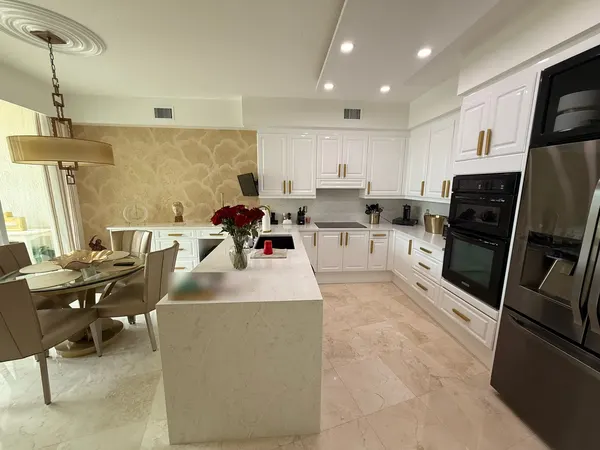 Finished white kitchen with gold hardware, built-in wall ovens and a waterfall island.