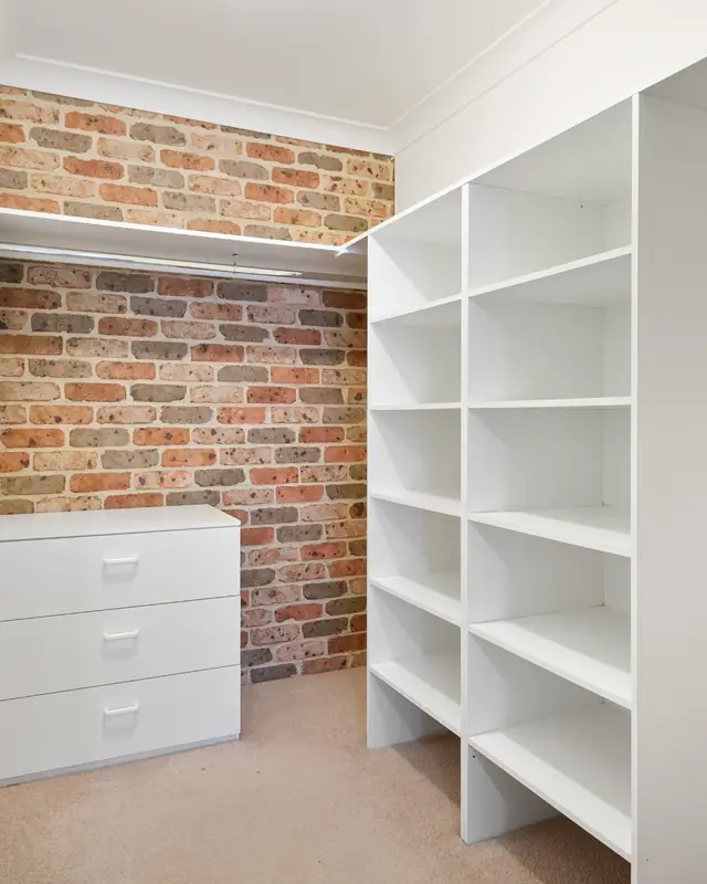 White closet shelving next to a brick wall