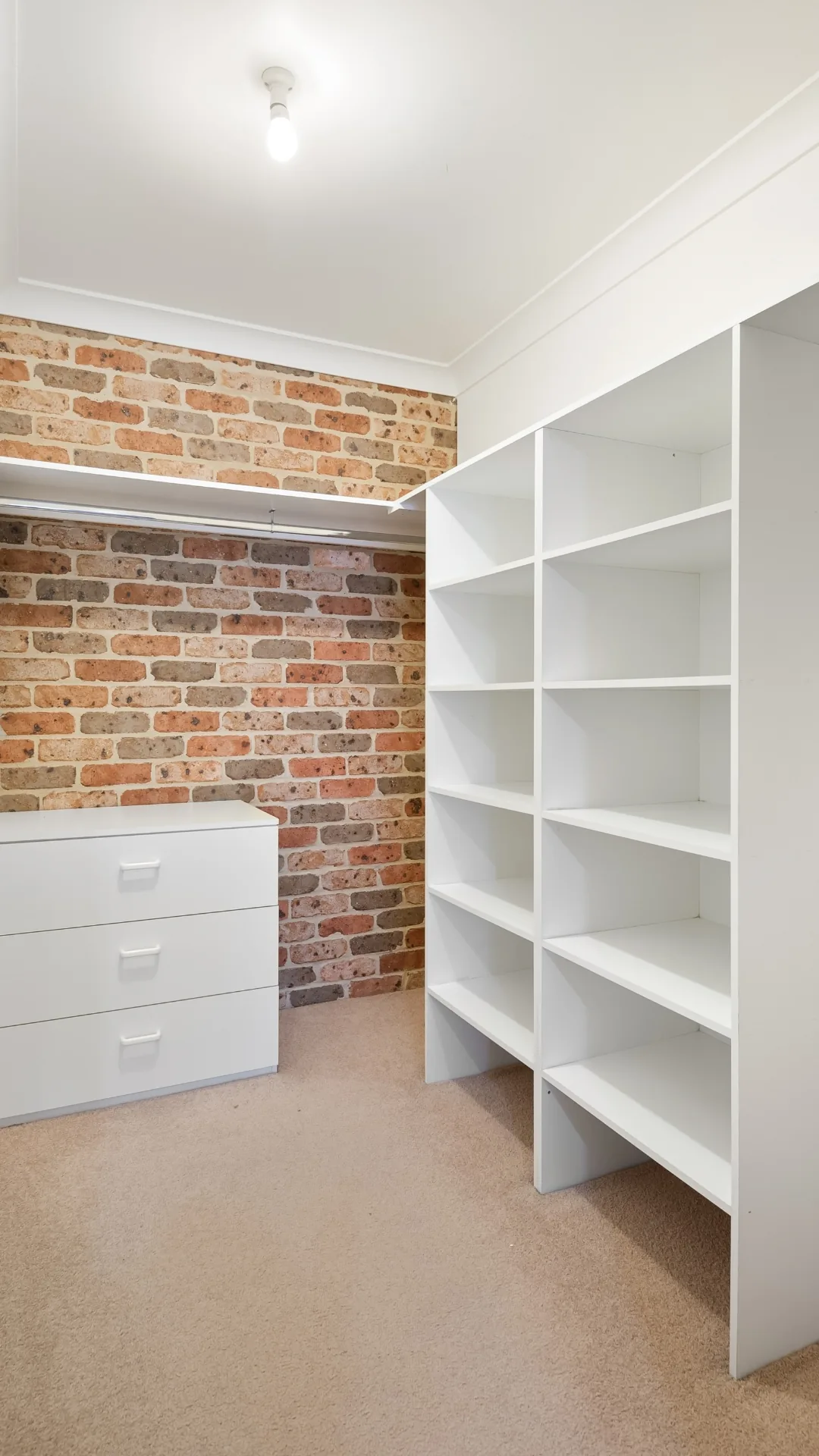 White closet shelving next to an exposed brick wall