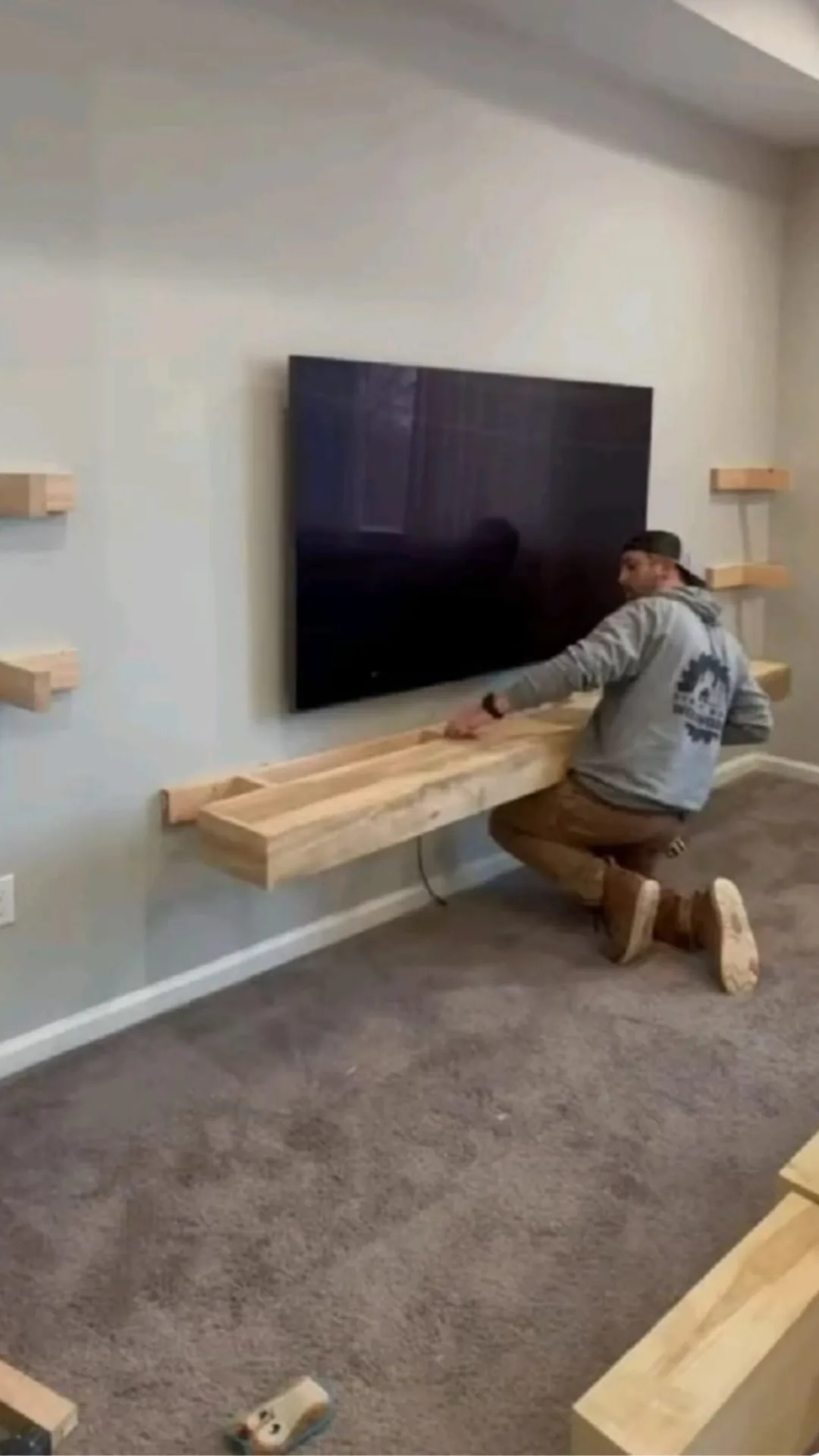 Carpenter installing a floating wood shelf under a wall-mounted TV