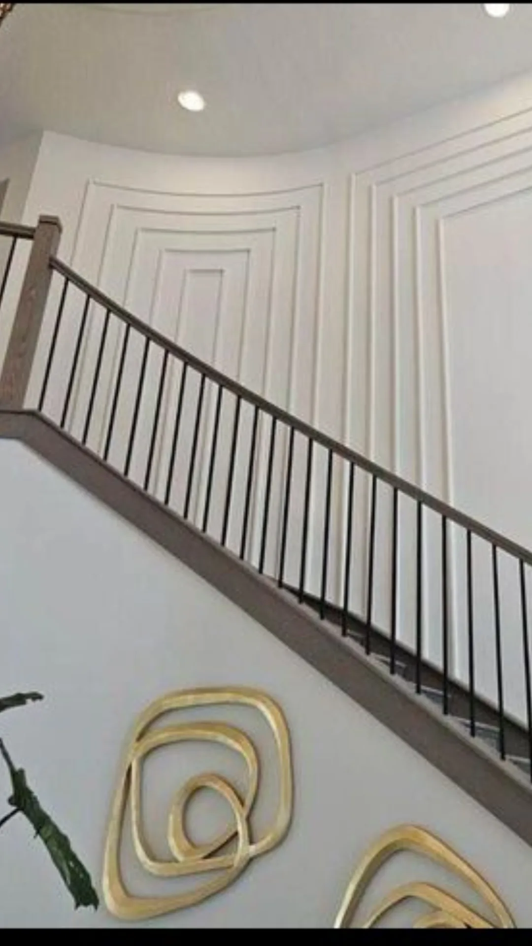 Staircase with black metal railing and paneled wall